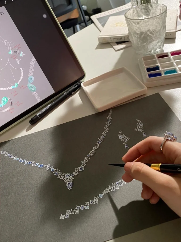 A hand sketching jewelry details alongside reference drawings.